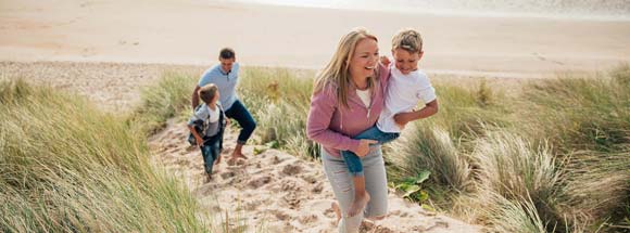 Mother carrying child up sand dune as father and son trail behind on beach