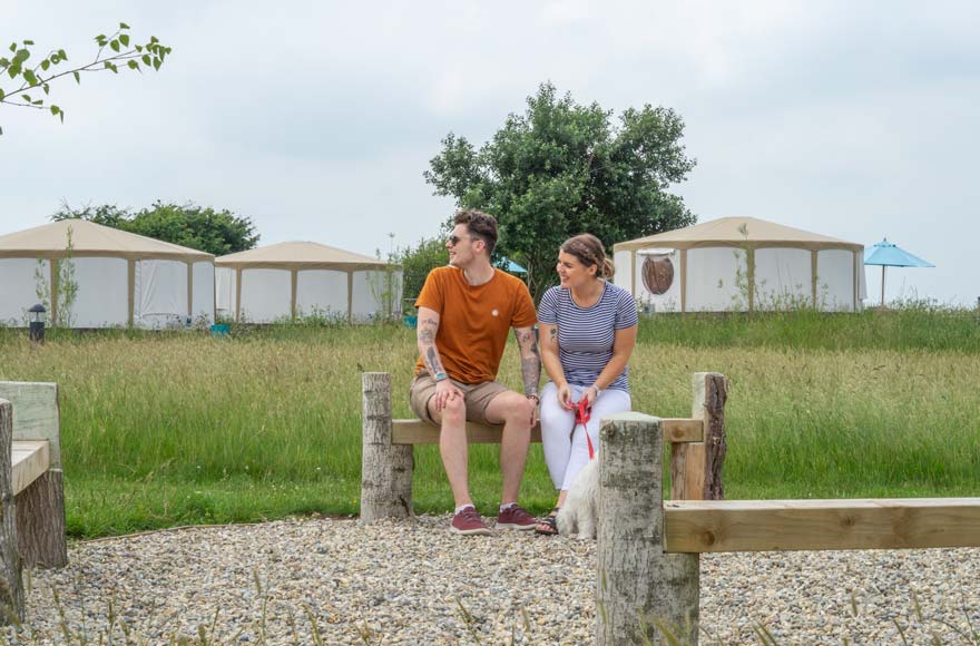 Couple with dog sitting outside three yurts in countryside