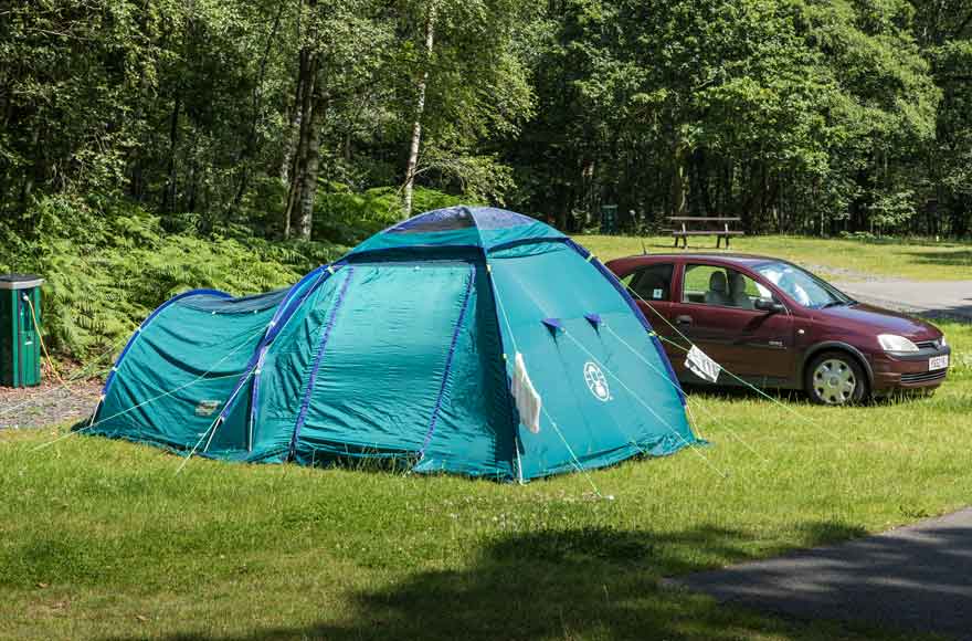 Blue tent pitched next to dark red car near trees
