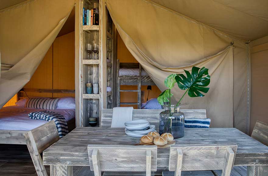 Wooden table and chairs inside spacious safari tent with 3 beds